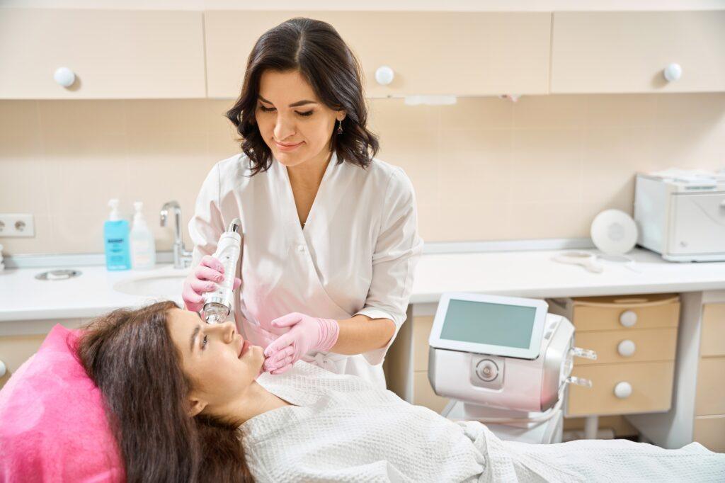 Qualified dermatologist carrying out RF microneedling on young woman